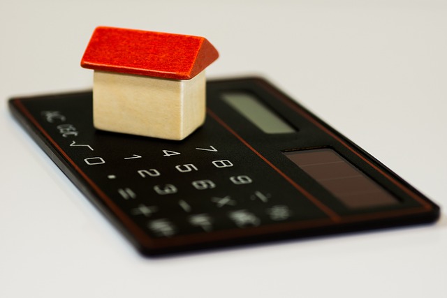 a small toy house made of wood with a red roof sits on a black calculator on a white background